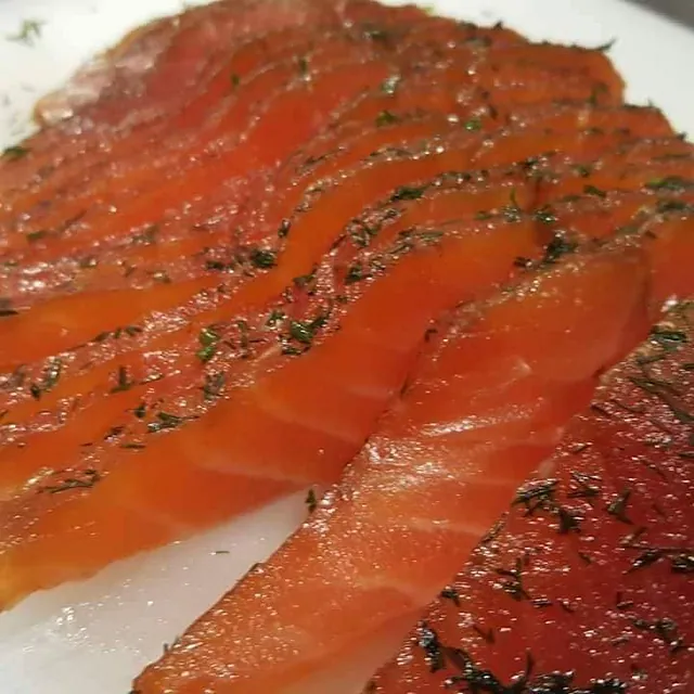Tynne skiver av gravlaks med dill, pent lagt på hvit tallerken.
